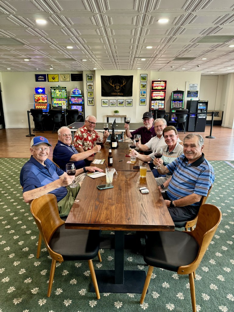 A group of 7 men enjoy a round of beers and wine at the clubhouse.